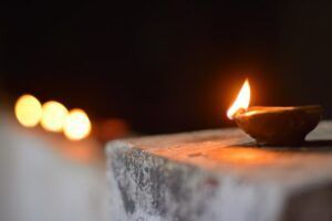 Lit oil lamp on a stone ledge with blurred candle lights in the background.