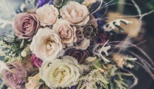 Bouquet of pale pink, cream, and lavender roses with greenery on a dark background