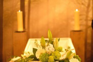 Candles flanking a white floral arrangement on a warm-lit altar or ceremonial table