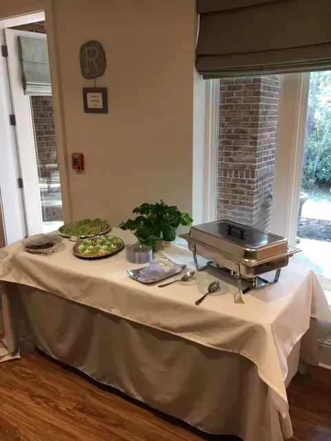Buffet table with white cloth, serving dishes, salad bowls, and a chafing tray by a window