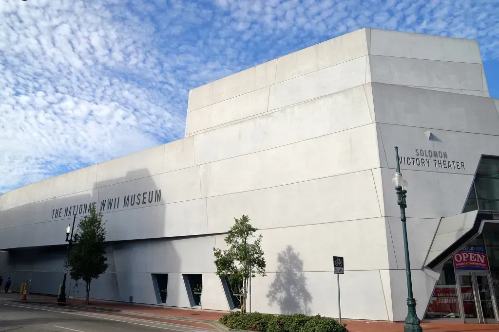 Modern white museum building under a blue sky, with trees and a sidewalk in front