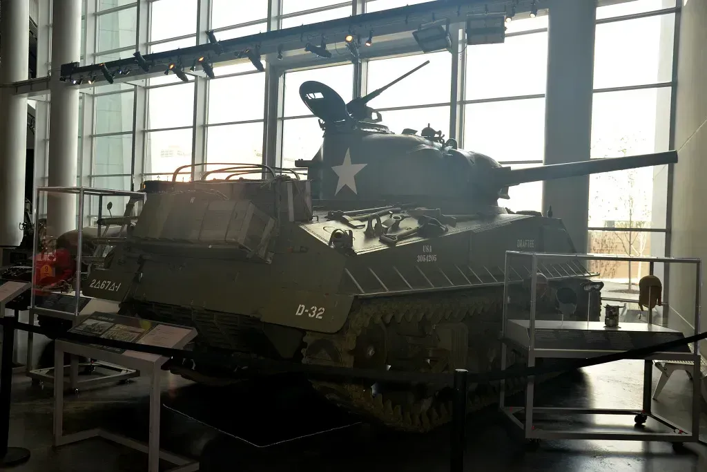 Military tank displayed indoors in a large glass-walled museum or hangar
