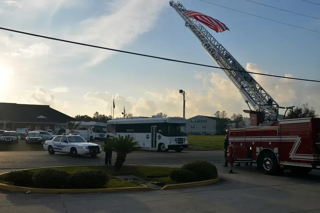 Fire truck with extended ladder and American flag at a parking lot entrance at dusk