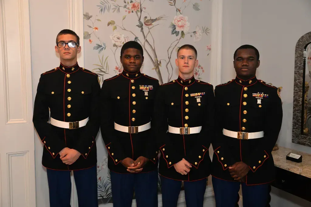 Four uniformed military members standing indoors against floral wallpaper