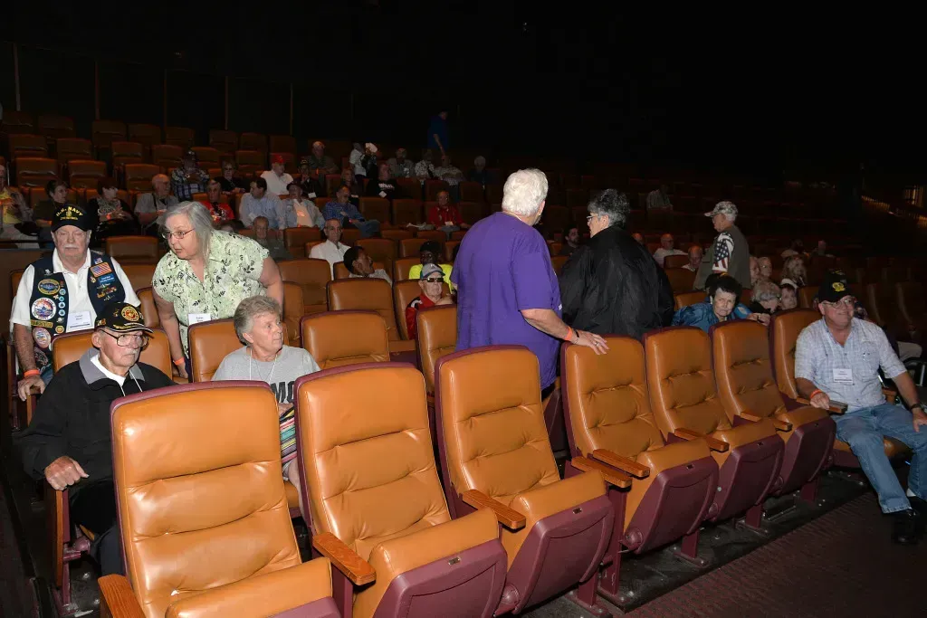 Audience seated in an auditorium with orange chairs, facing a dark stage