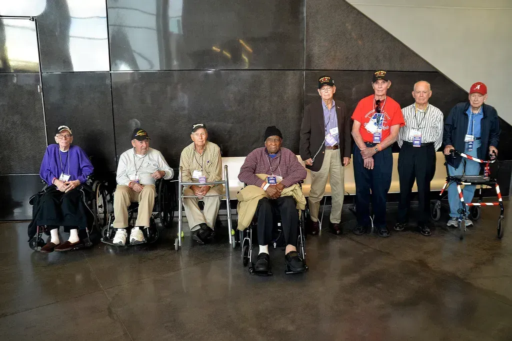 Group of people seated in a lobby, some using wheelchairs and mobility aids, posing for a photo
