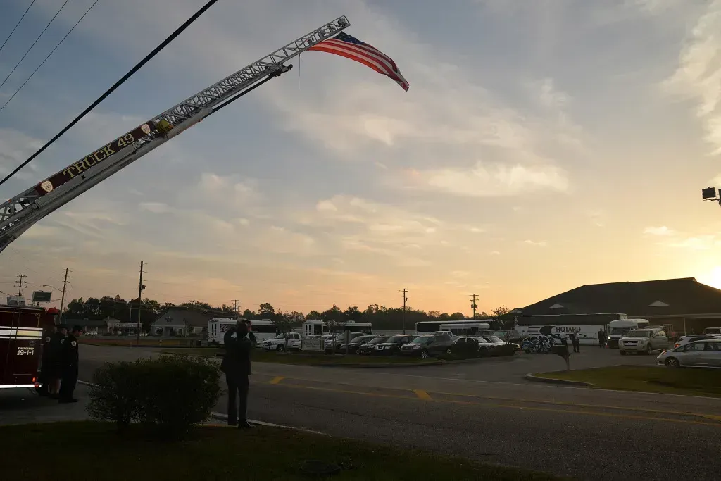 Fire truck ladder hoists a large American flag over a parking lot at sunset