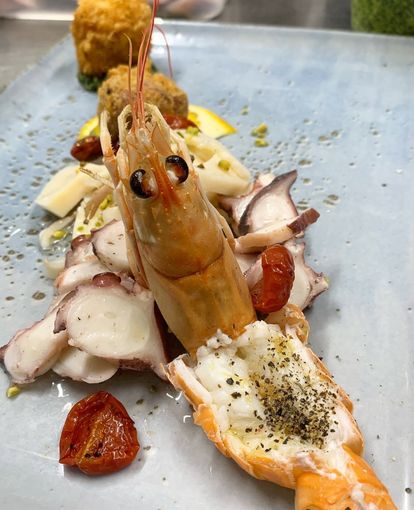 Antipasto di frutti di mare con gamberi, polpo a fette, pomodorini e erbe aromatiche su un piatto bianco.