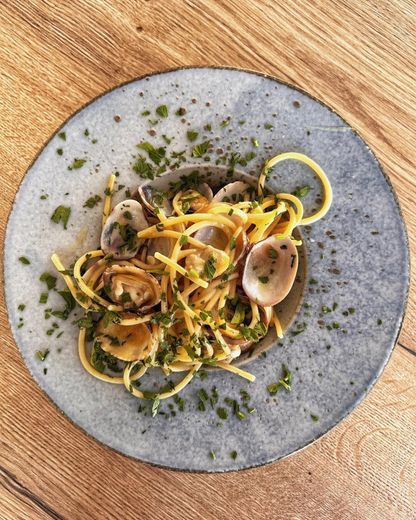 Piatto di vongole con guarnizione di erbe aromatiche e scorze di limone, adagiato su un piatto grigio su un tavolo di legno.