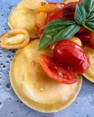 Ravioli conditi con pomodorini, foglie di basilico e una leggera glassa all'olio d'oliva.