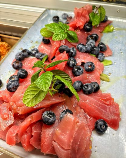 Fette di frutta rossa disposte su un vassoio, guarnite con mirtilli e foglie di menta.