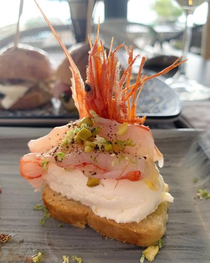 Antipasto di toast di gamberi con crema spalmabile ed erbe aromatiche su un piatto scuro, servito a un tavolo all'aperto.