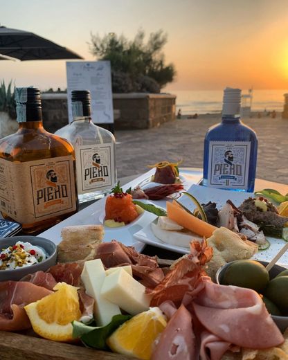 Piatto di frutti di mare con bottiglie di Piena su un tavolo in riva al mare al tramonto.