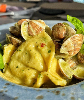 Ravioli in salsa cremosa con vongole e basilico in una ciotola blu