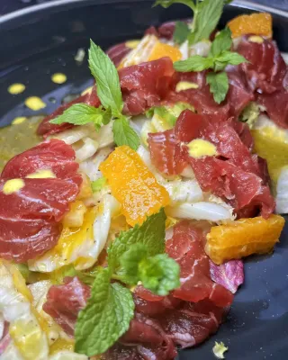 Insalata fresca da dessert con menta, scorza d'arancia e frutti rossi su un piatto nero.