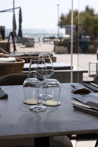 Tavolino da caffè all'aperto con bicchieri e menù dei vini, affacciato su un luminoso patio sul mare.