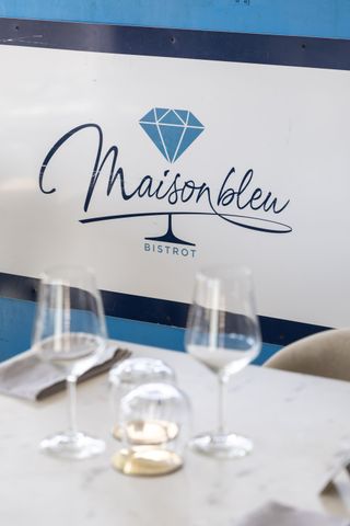 Insegna del bistrot Maison bleu su una parete blu e bianca dietro un set di bicchieri da pranzo.