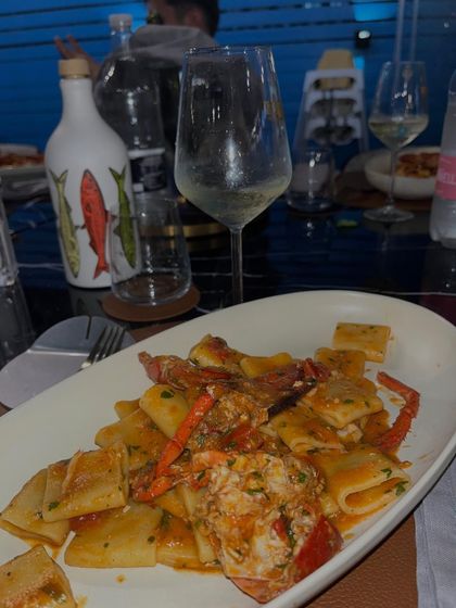 Pasta ai frutti di mare su un piatto bianco, con bicchieri e bottiglie su un tavolo di ristorante.