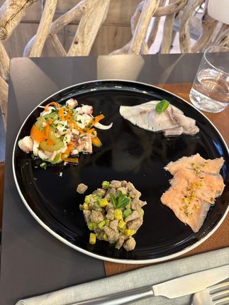 Un piatto nero con tre piccoli antipasti e un bicchiere d'acqua su un tavolo.