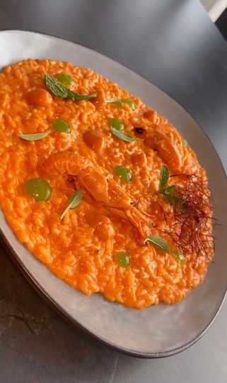 Risotto cremoso all'arancia su un piatto grigio, guarnito con erbe aromatiche e un filo d'olio.