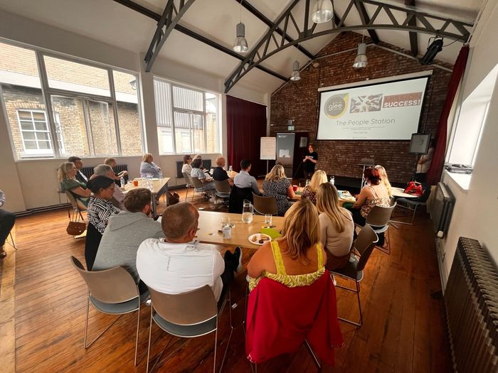 A large room with people sitting at desks watching someone present information on a large screen