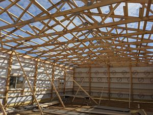 Wooden roof trusses under construction at a building site, with scaffolding and sunlit open walls.