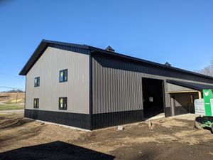 New gray metal building with black trim on a dirt lot under a clear blue sky