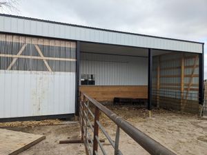 Open barn stalls with metal siding, wooden bench, and rusty fence under a cloudy sky