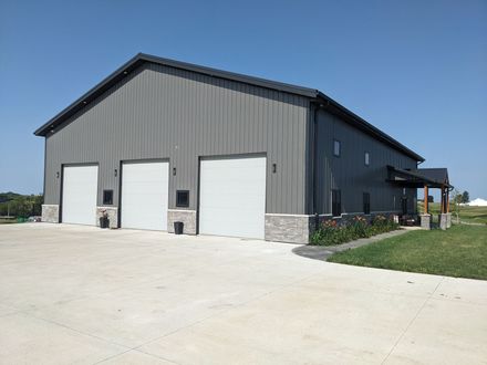 Gray metal barn with three white garage doors on a concrete driveway under a clear blue sky