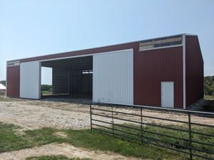 Large red-and-white barn with open doors on a gravel lot behind a black fence