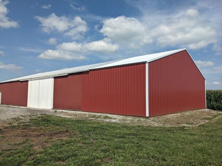 Red metal barn with white doors on a grassy lot under a partly cloudy sky