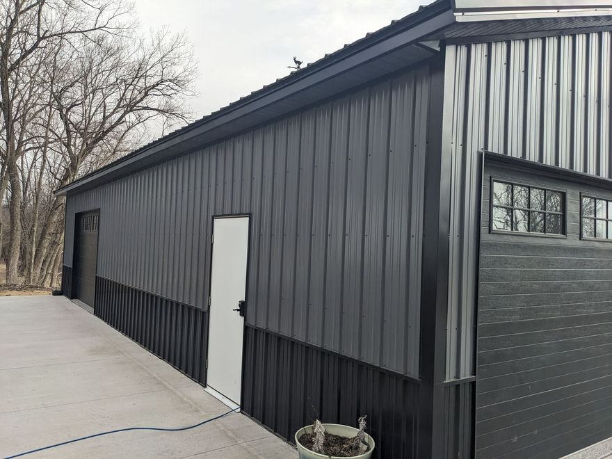 Black metal-sided building with a white door and small windows along a paved driveway