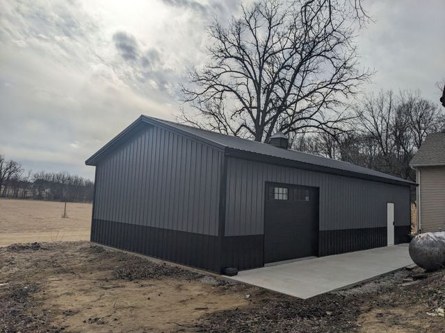 Dark gray metal shed with a concrete pad in a rural field under a cloudy sky
