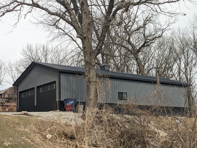 Gray industrial building beside leafless trees on a rural lot under an overcast sky