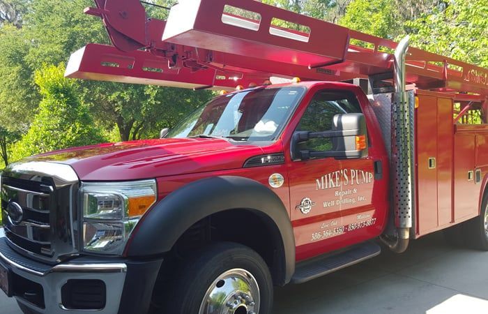 Red work truck with a ladder, parked outdoors.