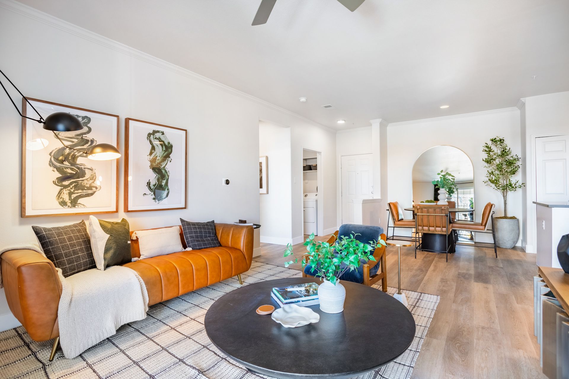 Living room with tan leather sofa, artwork, rug, round coffee table, and dining area.