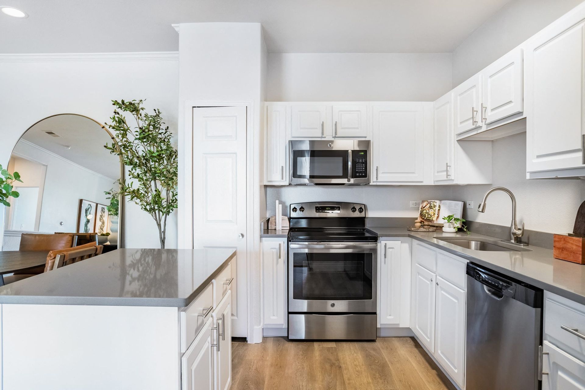 Modern, white kitchen with stainless steel appliances, gray countertops, and light wood flooring.