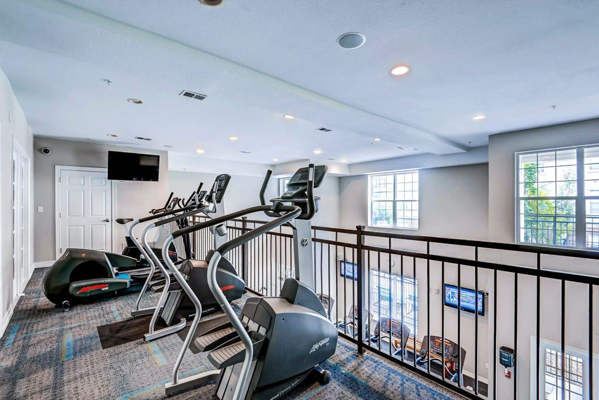 Gym with elliptical machines, overlooks a lower level. White walls, blue carpet.