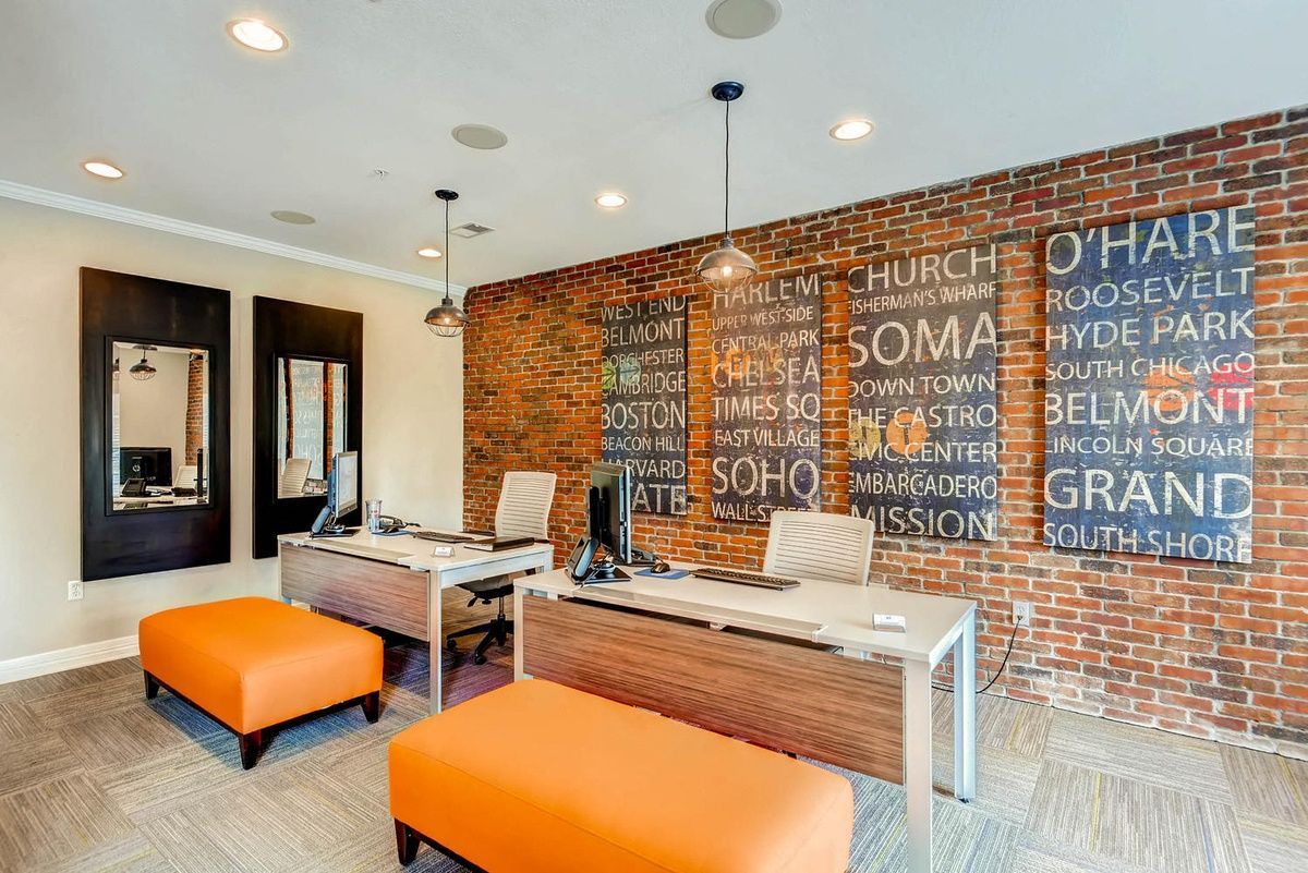 Office reception with brick accent wall, desks, and orange ottomans.