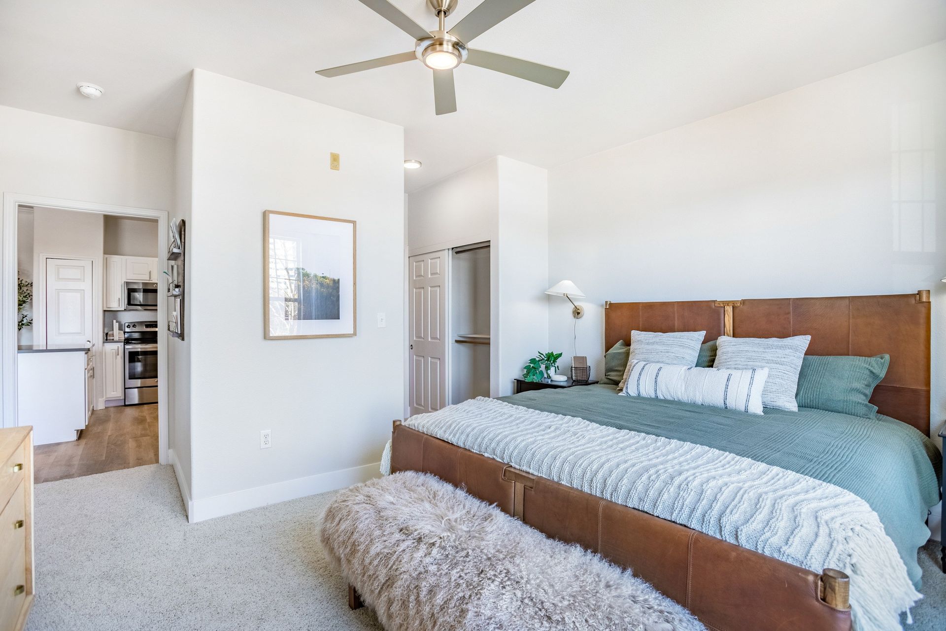Bedroom with leather bed, green bedding, fluffy bench, and access to a kitchen.