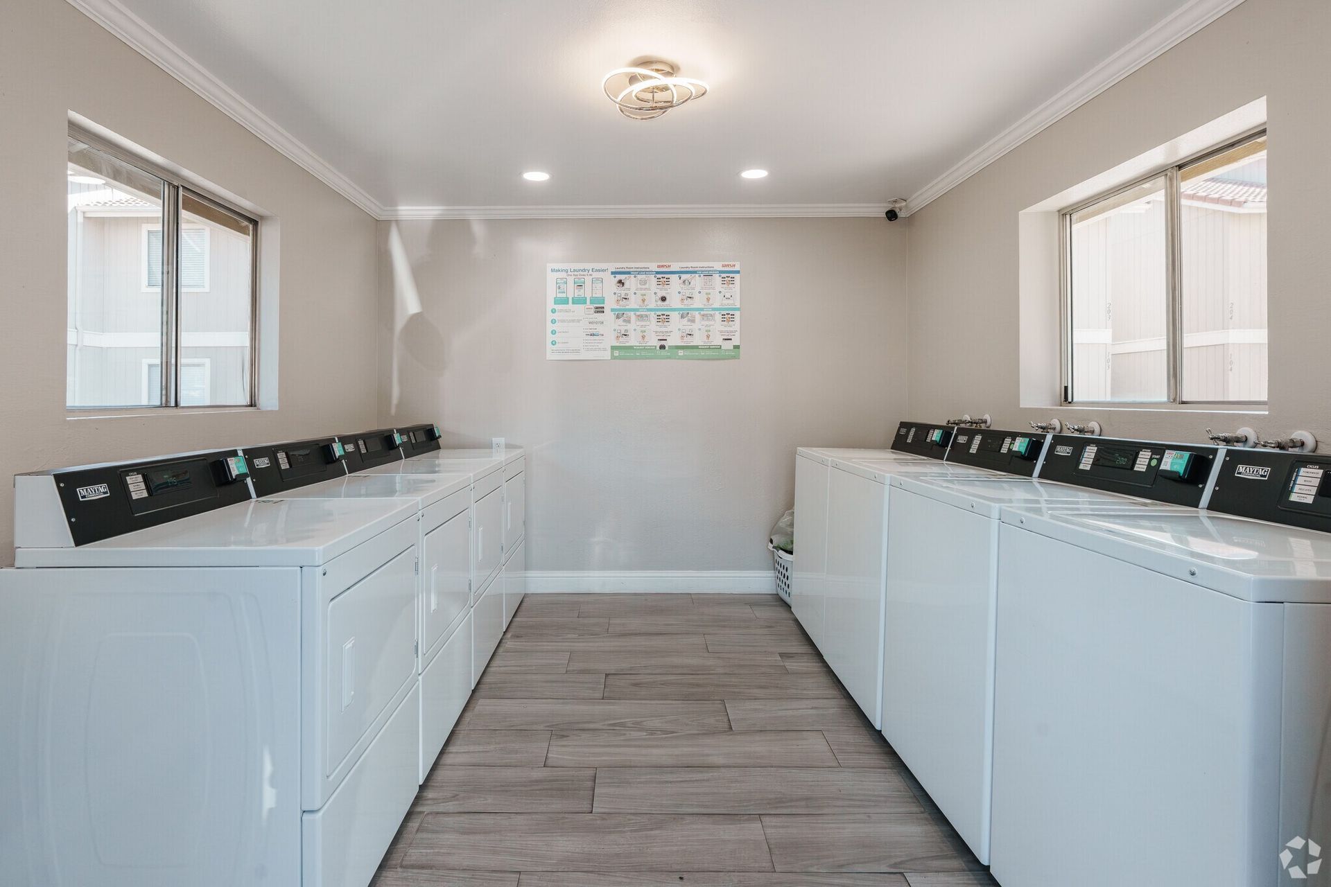 Laundry room with white machines, wood-look floor, windows, and instructions on the wall.