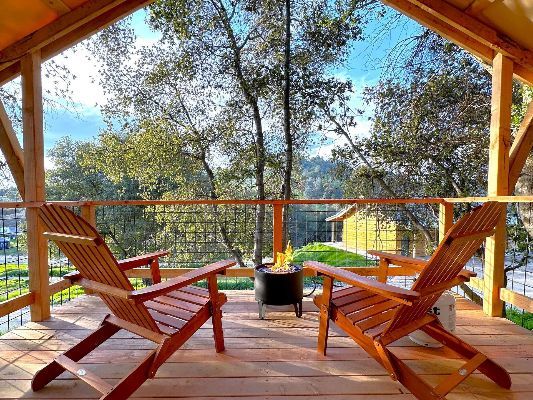Two wooden chairs are sitting on a wooden deck with a fire pit.