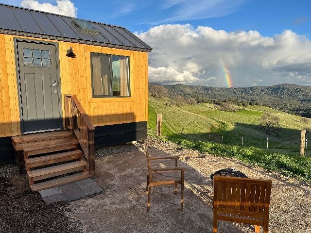 A small house is sitting on top of a dirt hill with a rainbow in the background.