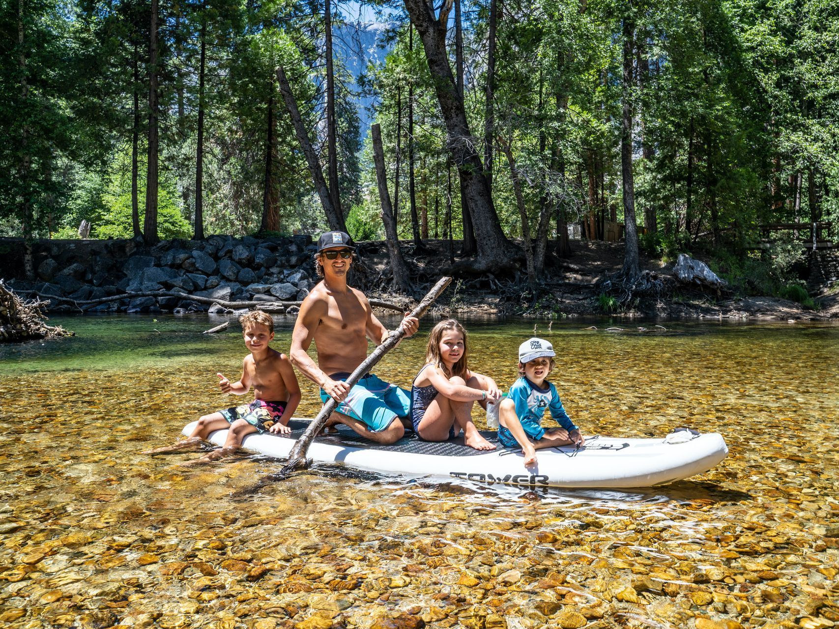 A man and three children are sitting on a paddle board in a river.