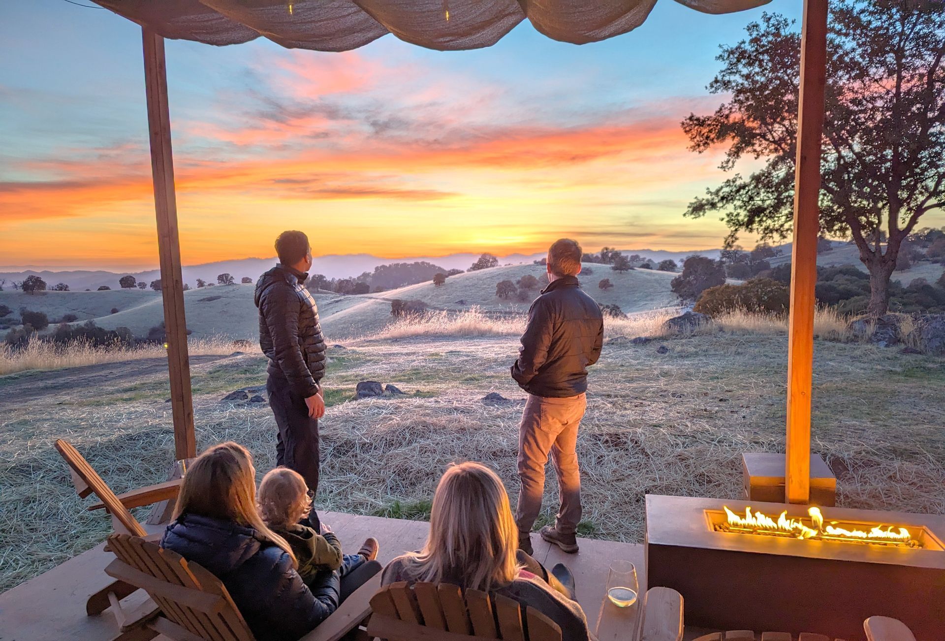 A group of people are sitting on a porch looking at the sunset.