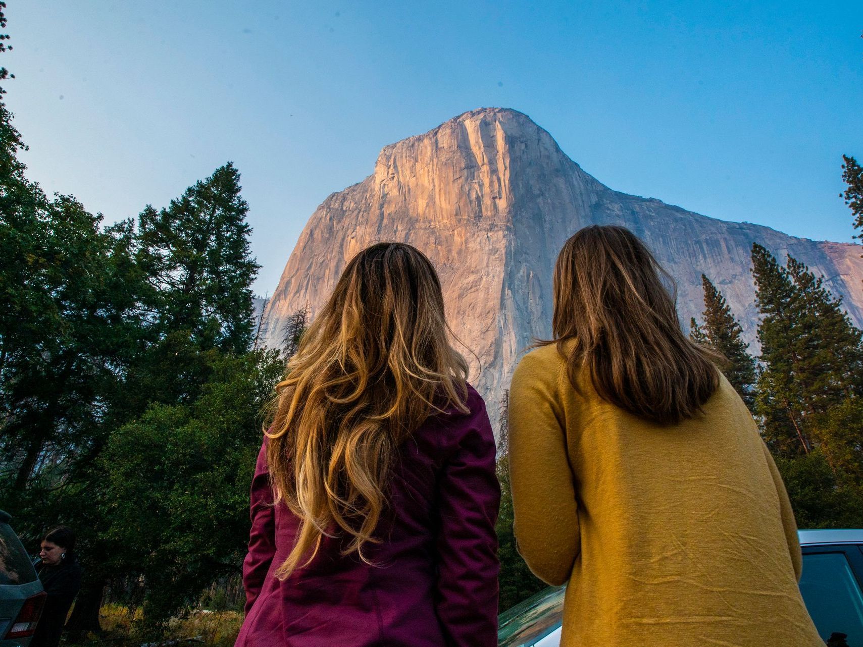 Two women are standing next to each other looking at a mountain.