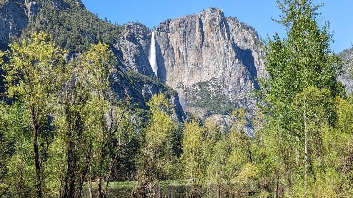 A waterfall is surrounded by trees and mountains in the background.
