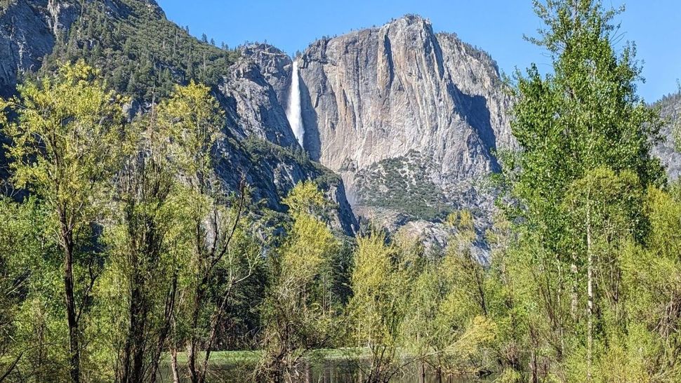 A waterfall is surrounded by trees and mountains in the background.