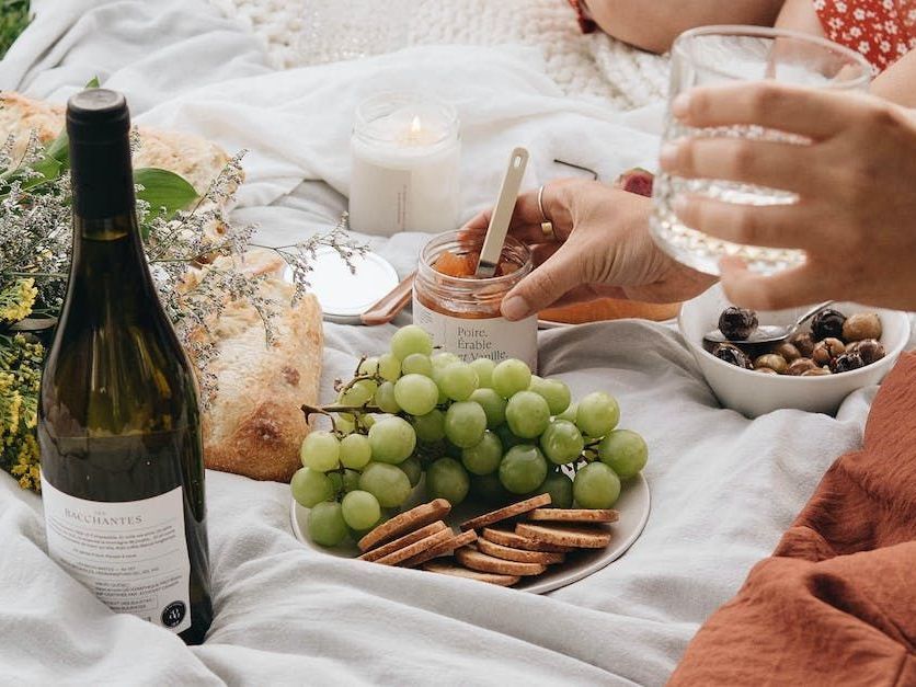A person is having a picnic with a bottle of wine , grapes , crackers and nuts.
