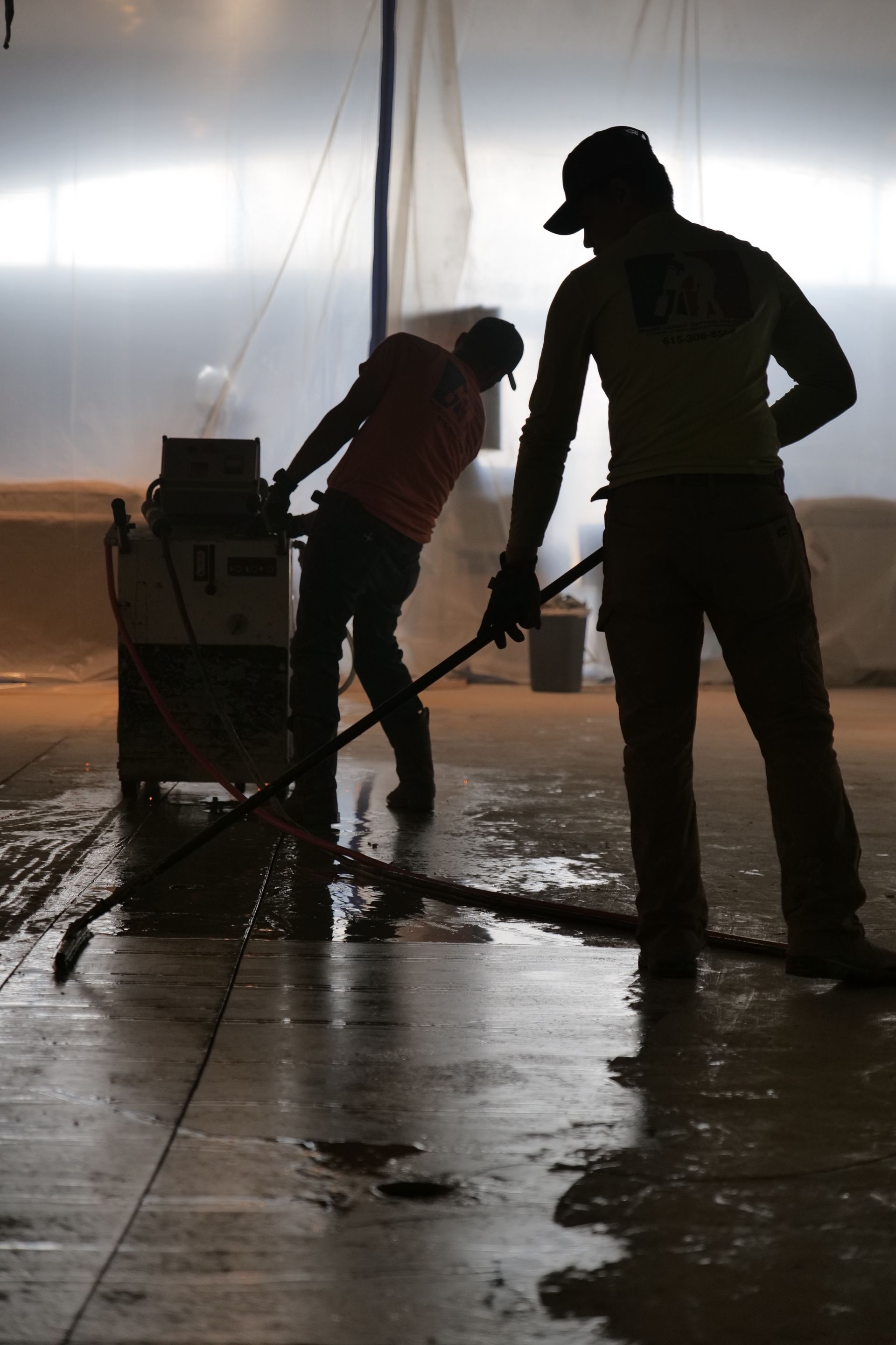 Two men are cleaning a floor with a mop as the cut concrete